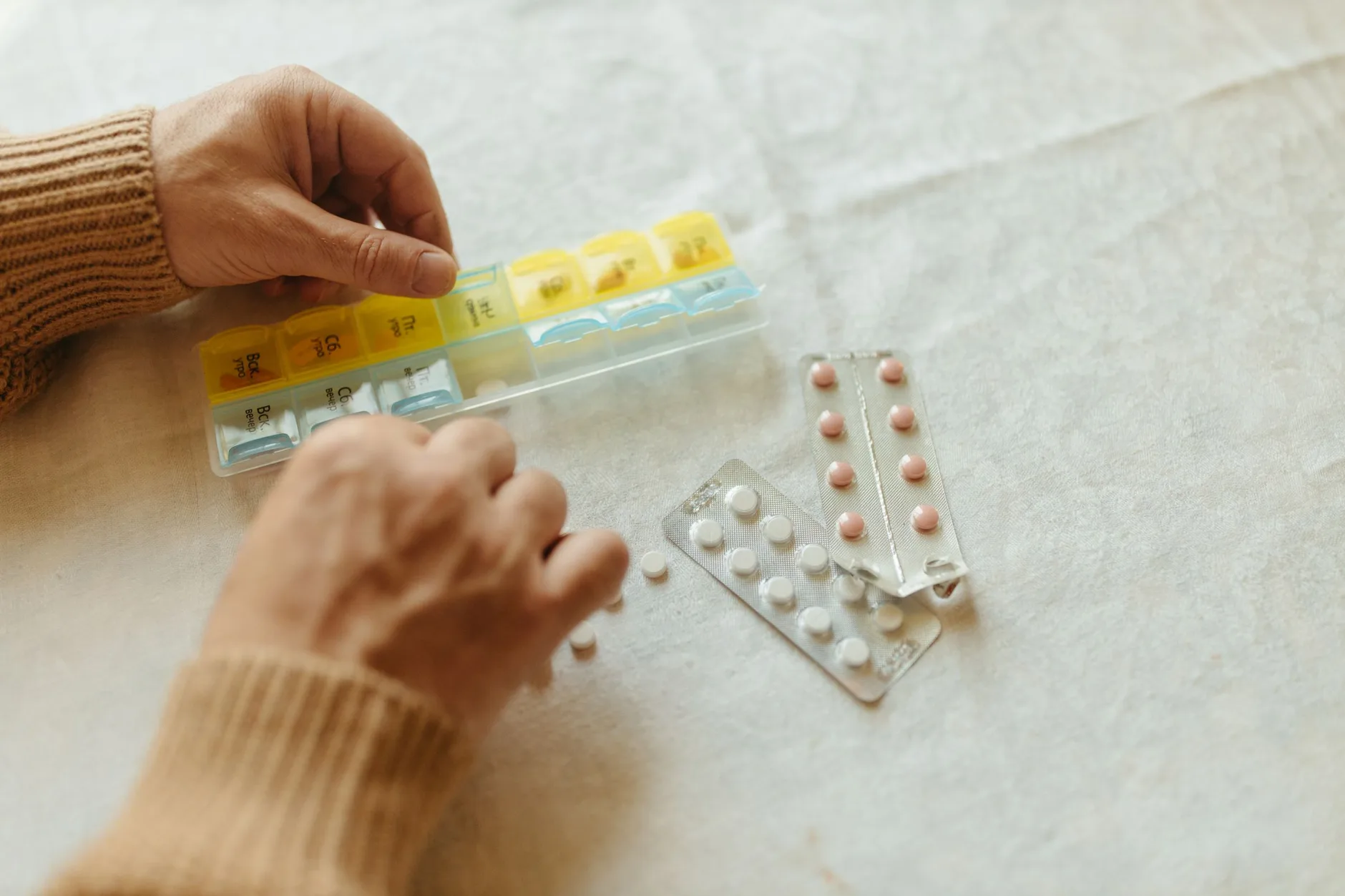 Una persona con Medicare organizando sus recetas en un pastillero semanal en casa